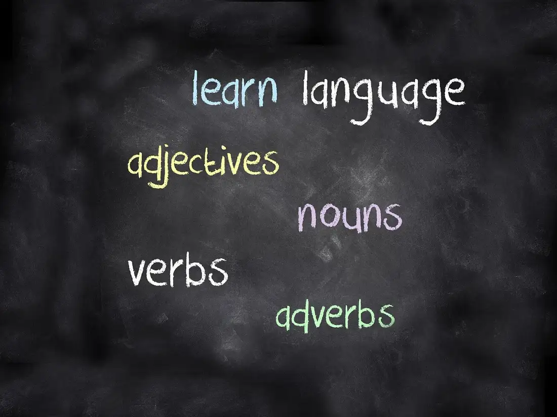 A chalkboard covered in language-learning terms: nouns, verbs, adjectives, adverbs