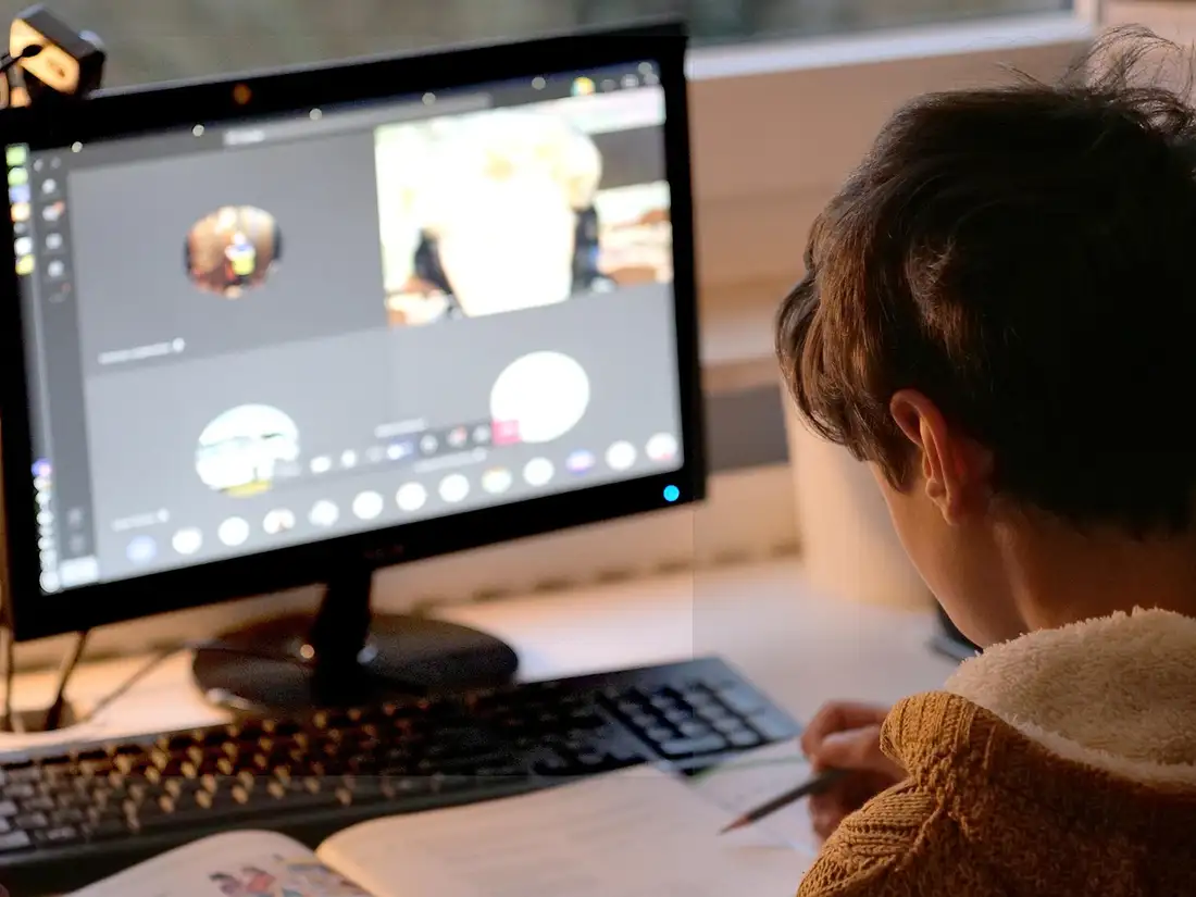 A learner writing at a desk in front of a screen during a one-to-one online lesson