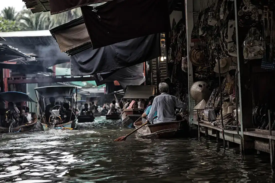 A boatman paddling through a crowded Thai floating market lined with stalls