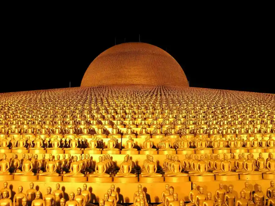 Rows of small golden Buddha statues lit at night, the tradition of respect the wai comes from