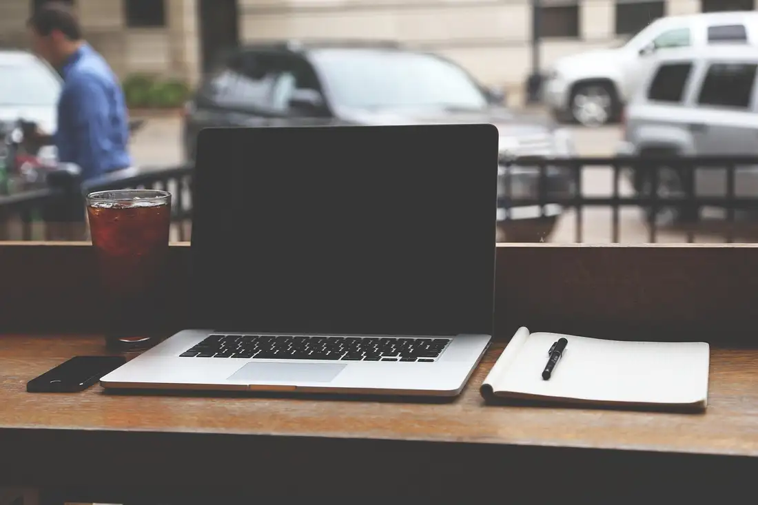 An open laptop, notepad and iced drink on an outdoor table, a daily Thai study session