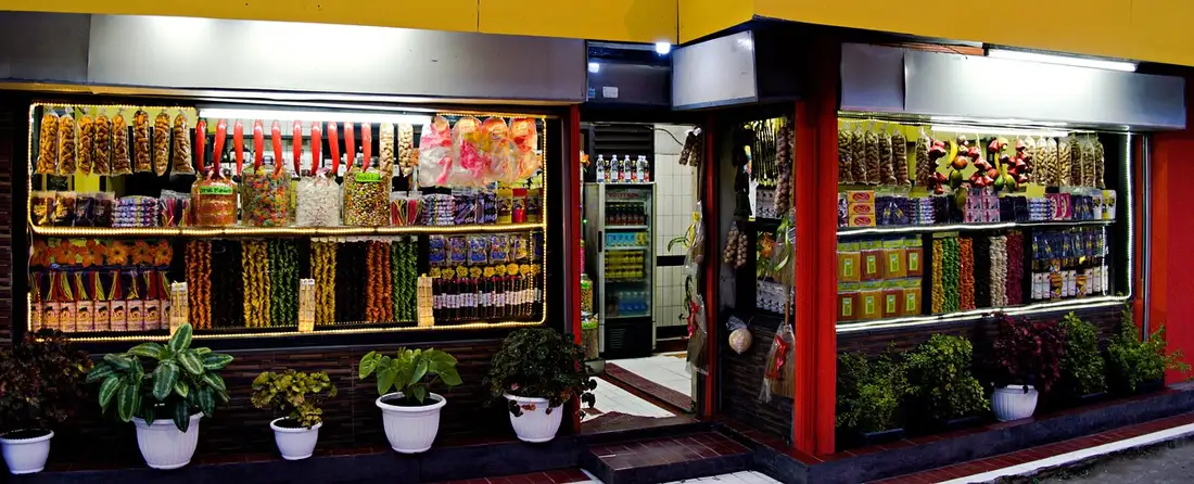 A lit shopfront at night selling dried snacks and sweets, an everyday place to say hello in Thai