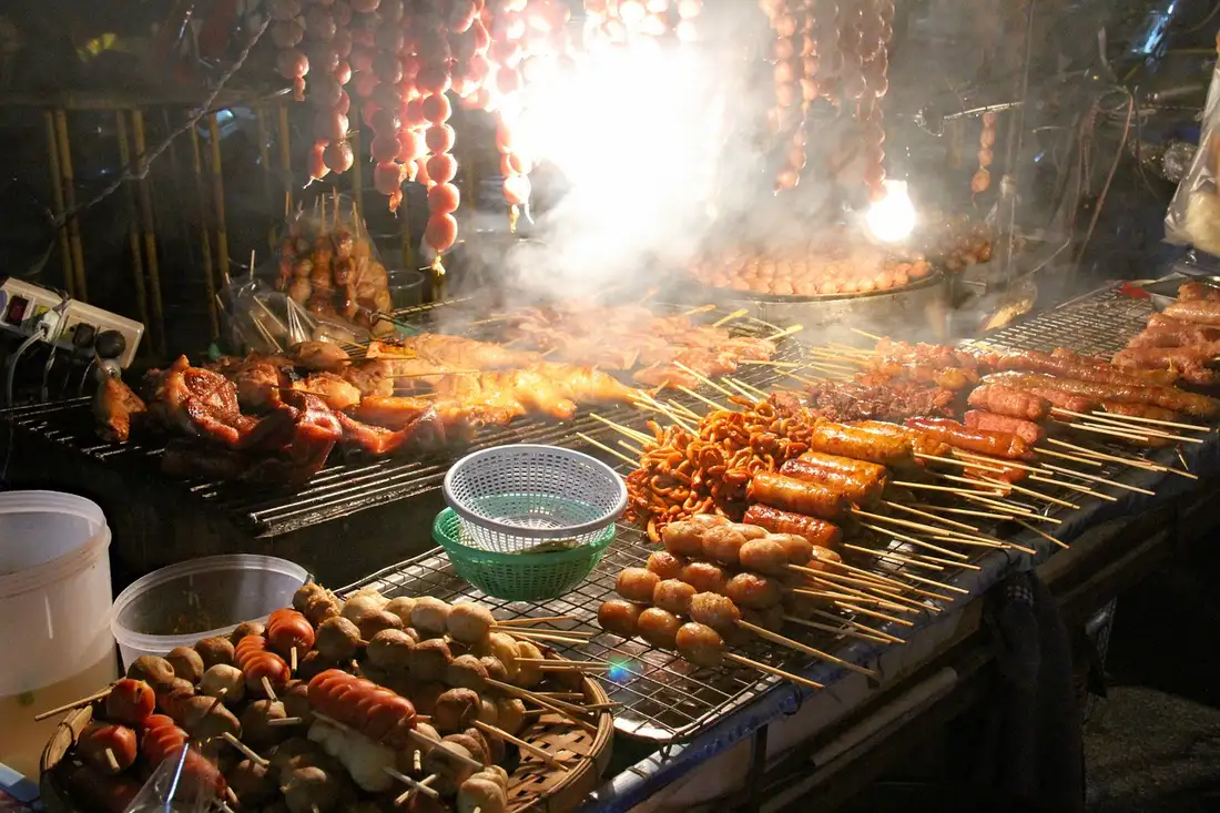 A night street grill in Thailand with skewered sausages and meatballs steaming