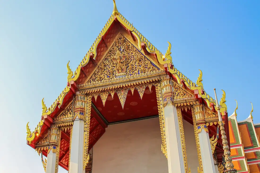 A gilded Thai temple gable and roof finials against a blue sky, where sawasdee has its roots