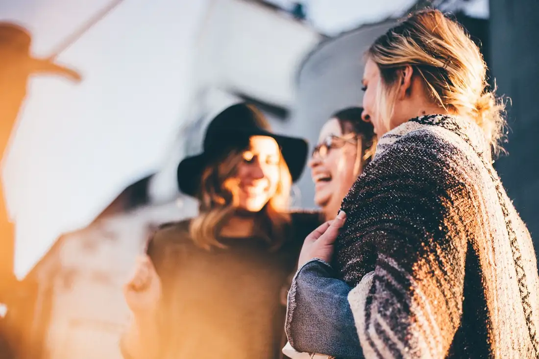 Three women laughing together outdoors in warm light, practising conversation
